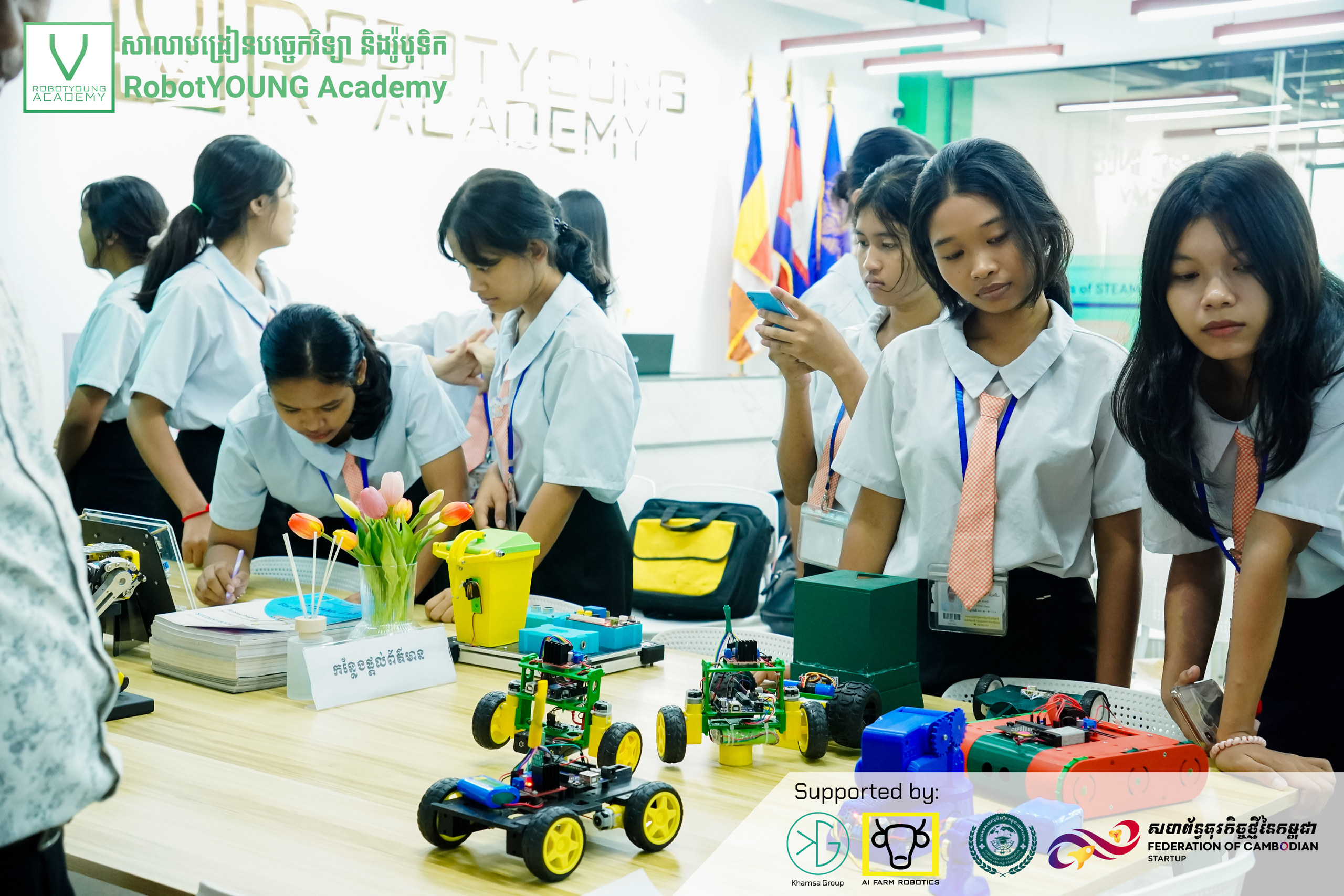 Students examining colorful wheeled robots displayed on a classroom table