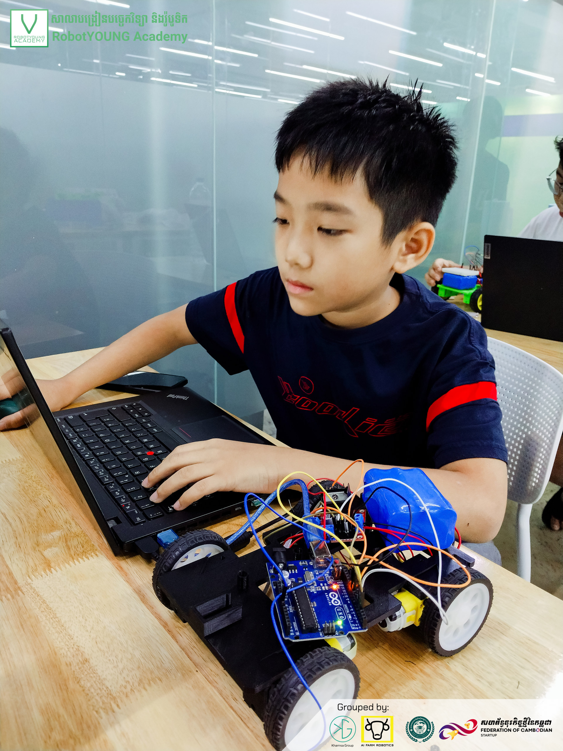 A student using a laptop beside a blue wheeled robot with exposed wiring